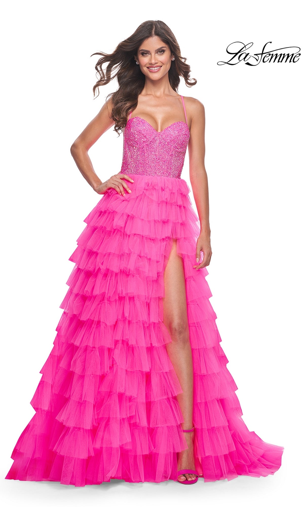 A woman stands smiling in the La Femme Long Tiered A-Line Prom Dress 32335, a bright pink strapless gown with a beaded sweetheart corset and a high-slit tiered skirt.